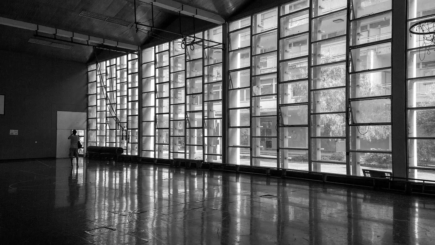 Leere Sporthalle mit Fensterfront und spiegelndem Hallenboden vor dem Anwurf